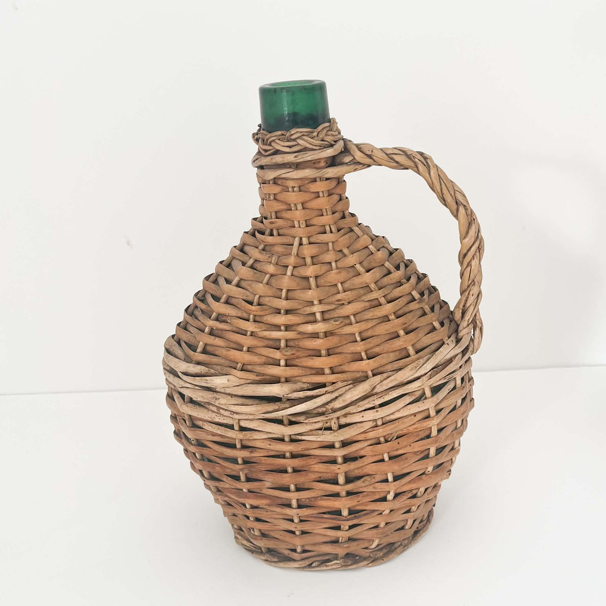 Traditional European glass demijohn covered in handwoven willow wicker, featuring warm natural tones and beautiful vintage craftsmanship