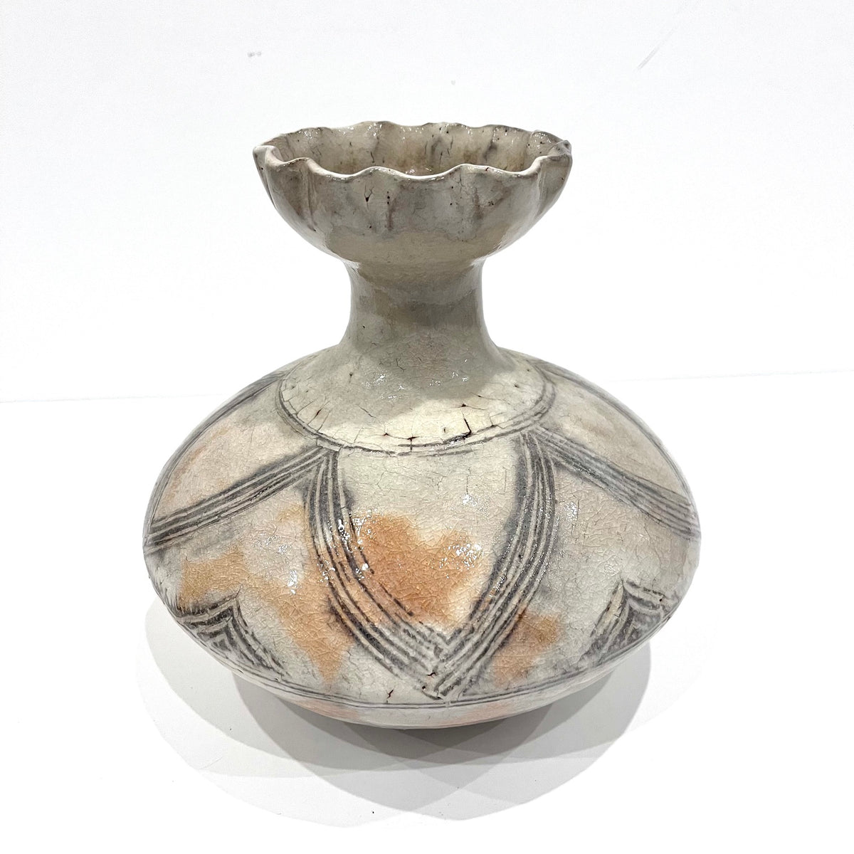 A vintage ceramic vase with a bulbous rounded body, a narrow neck, and a scalloped rim, decorated with black geometric lines over a warm beige and brown glaze on a white background.