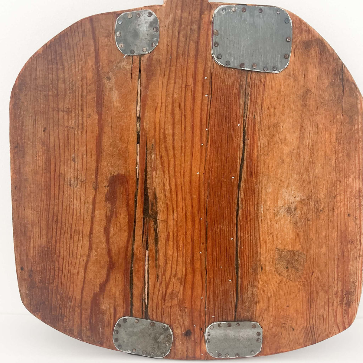 Antique European bread board featuring rustic metal repair patches that add character to the aged solid wood