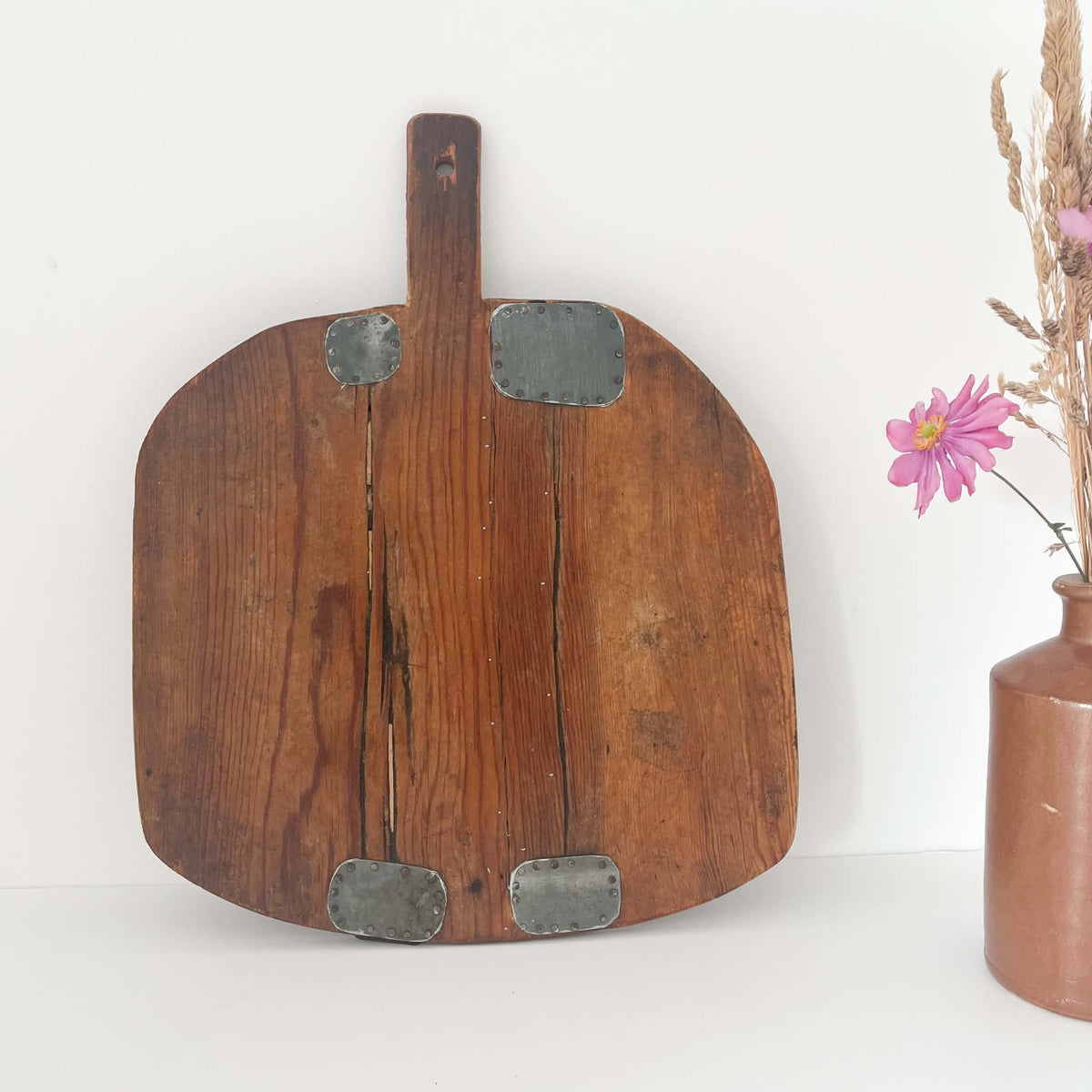 Reverse side of an antique wooden bread board showing aged wood grain, rustic metal mending patches and natural wear